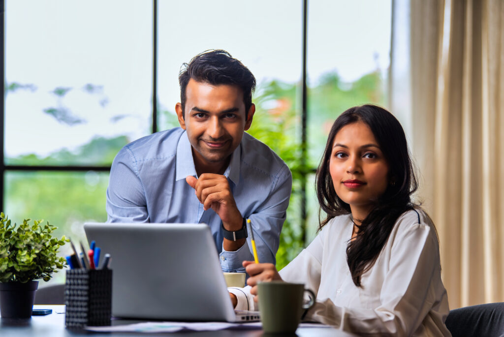 indian coworkers in formal dress work on project at desk with laptop and papers in office setting